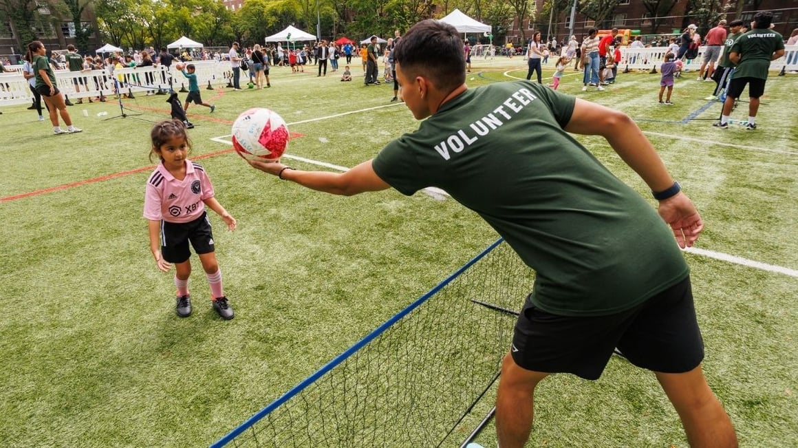 A Big Kick 2024 volunteer pictured handing a soccer ball to a young attendee